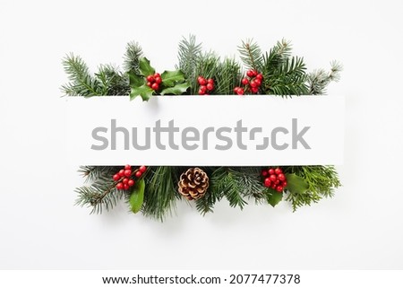 Composition of red holly berries and green branches on white background. Winter natural decoration. Botanical festive flat lay, top view.