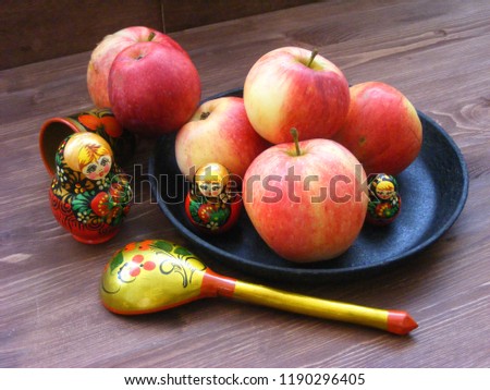 composition of red and yellow apples on black cast iron plate with traditional russian nesting dolls matrioshka and painted spoon on brown wooden table