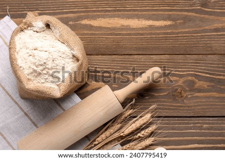 Composition with sack bag of flour, rolling pin and wheat ears on wooden table