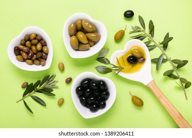 Composition seen from above with heart-shaped ceramic bowls, extra virgin olive oil, some types of olives and olive branch on a uniform green background.