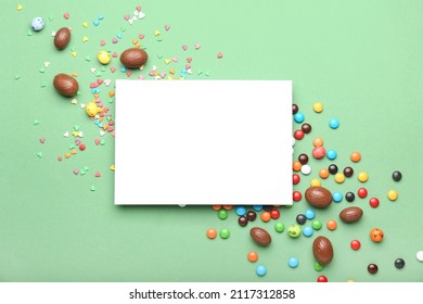 Composition with sheet of paper, chocolate Easter eggs and candies on green background