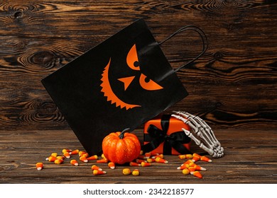 Composition with shopping bag, skeleton hand, gift box and tasty candy corns for Halloween on wooden background
