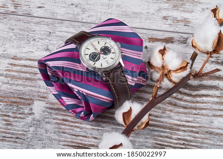 Composition of spring accessories on a white table. Rolled up tie with handwatch and pussy wollow branch.