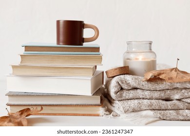 Composition with a stack of books, hot beverage in the mug and warm blanket. Cozy reading scene for cold weather with cup of coffee