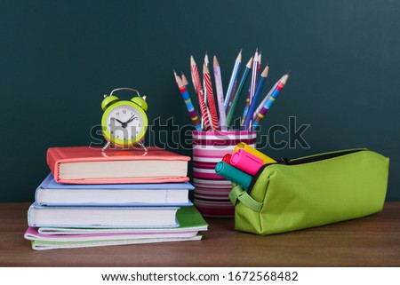 Composition with stationery and alarm clock on table near chalkboard. Doing homework