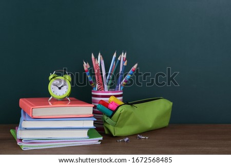 Composition with stationery and alarm clock on table near chalkboard, space for text. Doing homework