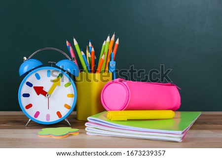 Composition with stationery and alarm clock on table near chalkboard. Doing homework