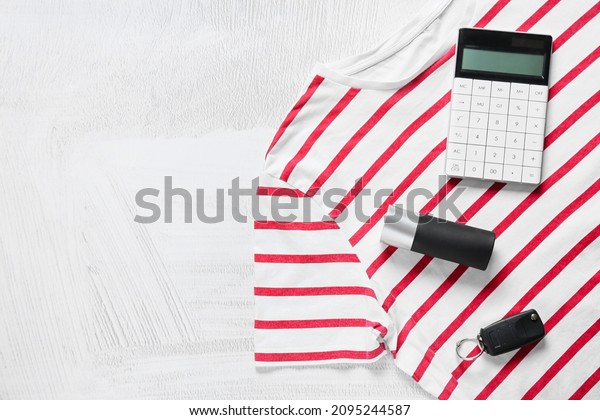 Composition with stylish t-shirt, car\
key, bottle of perfume and calculator on light\
background
