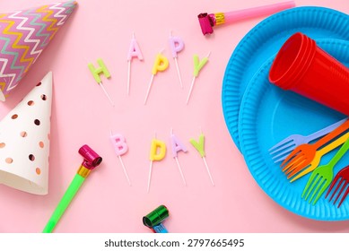 Composition with text HAPPY BDAY made of candles, paper tableware and party decor on pink background