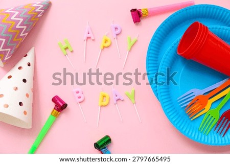 Composition with text HAPPY BDAY made of candles, paper tableware and party decor on pink background
