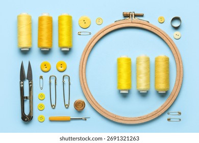Composition with thread spools, embroidery hoop, pins and buttons on blue background