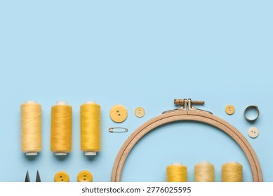 Composition with thread spools, embroidery hoop and buttons on blue background, closeup