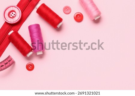 Composition with thread spools, zipper and buttons on pink background, closeup