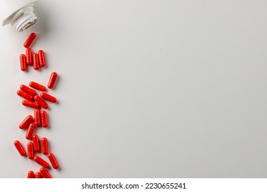 Composition of white pill box spilling red pills on white background with copy space. Medicine, medical services, healthcare and health awareness concept.