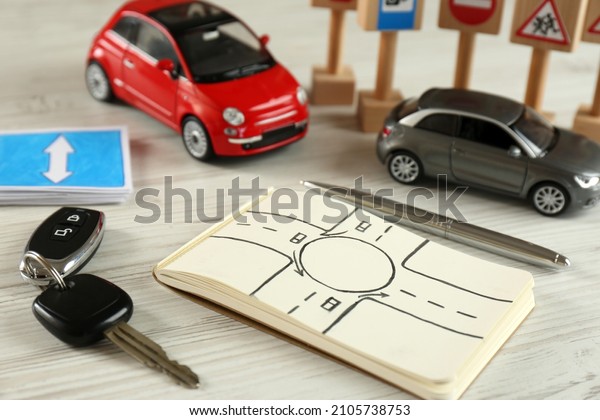Composition with\
workbook for driving lessons and toy cars on white wooden\
background. Passing license\
exam
