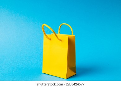 Composition Of Yellow Paper Shopping Bag On Blue Background. Retail, Shopping And Black Friday Concept.