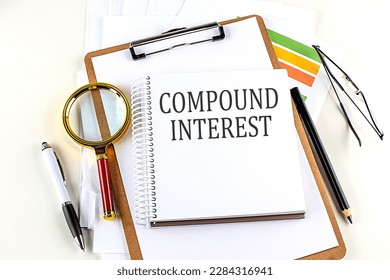COMPOUND INTEREST text on a notebook with clipboard on white background