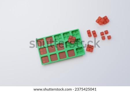 Compounded, red square flex dose troches (lozenges) in a green, plastic mold on a white countertop in a compounding pharmacy. Easy to taper and adjust dosing.