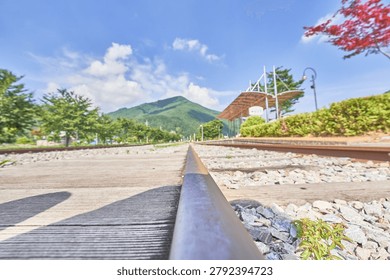        A comprehensive visual collection showcasing the contrasting day and night views of Najeon Station, a tranquil rural railway station in Jeongseon, South Korea. The daytime images feature a sunlit platform with a classic white station signboard, straight railway tracks, and lush green mountains under a bright blue sky with fluffy white clouds. The nighttime image captures the quaint station building with a red roof illuminated against a dark, starry sky with dramatic long-exposure clouds. This series beautifully captures the serene passage of time in a quiet countryside landscape.                       