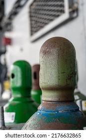 Compressed Gas Cylinders Being Stored Vertically Secured By A Metal Chain And A Metal Cap.