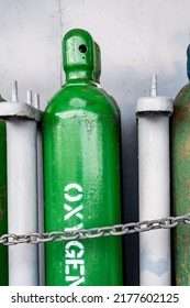 Compressed Gas Cylinders Being Stored Vertically Secured By A Metal Chain And A Metal Cap.