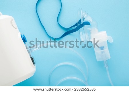 Compressor nebulizer and transparent mask with container for drug breathing on light blue table background. Closeup. Medical device for inhalation. Top view.