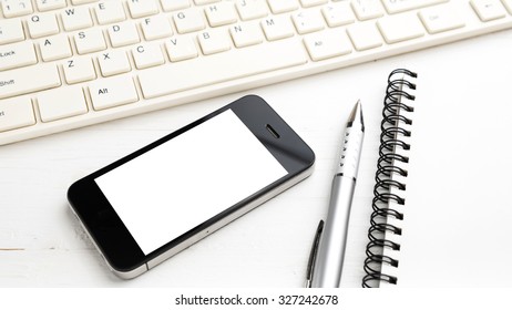 computer and cellphone with notebook and pen over white table