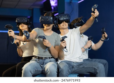 in computer club, group of four friends wearing virtual reality glasses and with joysticks are sitting and playing dynamic game with modern graphics. - Powered by Shutterstock