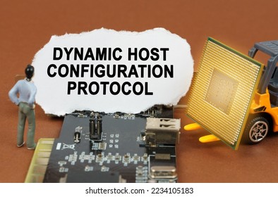 Computer concept. On the board with microcircuits lies a paper plate with the inscription - Dynamic Host Configuration Protocol. Nearby is a toy loader with a processor and a human figurine.