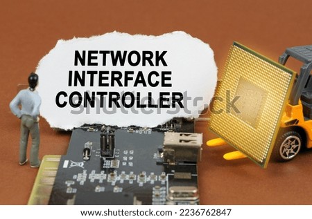 Computer concept. On the board with microcircuits lies a paper plate with the inscription - Network Interface Controller. Nearby is a toy loader with a processor and a human figurine.