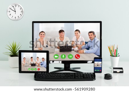 Computer Desktop With Digital Tablet And Mobilephone Showing Videoconferencing Application On Office Desk