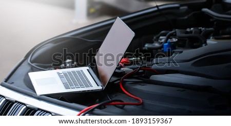 Computer diagnostics of the car in garage. Automotive mechanical technician using laptop computer programming and investing by car diagnostic software, car maintenance service concept.