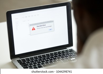 Computer error failure concept, african man using laptop with application failure message on screen, bad software pc app crash, email malware, data loss and recovery, rear view over the shoulder