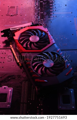 Computer game graphics card, videocard with two coolers on circuit board ,motherboard background. Close-up. With red-blue a lighting.