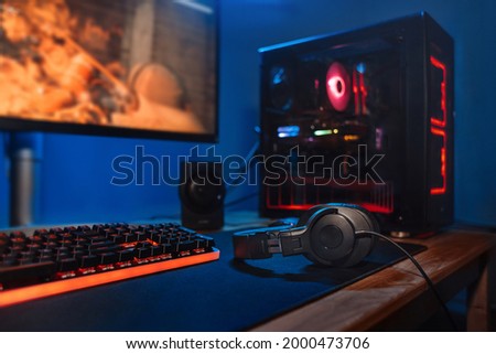 Computer gamer workplace with new game keyboard, mouse, headphones, modern pc with blur blue and red neon light. Powerful personal computer for e cyber sport gamer on the table at home. Close up