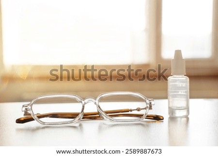 Computer glasses of blue light blocking, a small bottle of eye drops on a table near window. Eye care digital strain relief vision health eyewear impact of screen time on eye fatigue healthy habits