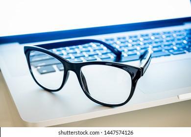 Computer Goggles On A Laptop, Close-up View. Blue Light Blockers Resting On Computer Keyboard, Eye Fatique Problem Concept