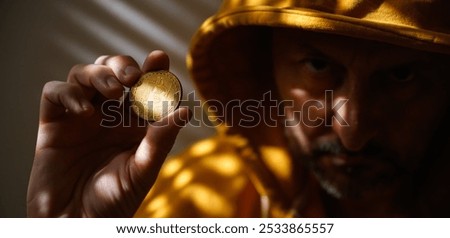 Computer hacker and cryptocurrency scammer in golden yellow hooded jacket holding Bitcoin in hand, selective focus
