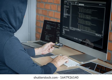 Computer hacker or cyber attack concept, Dangerous hooded hacker using multiple computers typing bad data into online system the access with a virus to infect steal information.