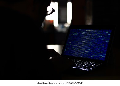 Computer Hacker silhouette typing on computer in a dark room. Working on blue binary code technology. binary data, computer programming and network security concepts.