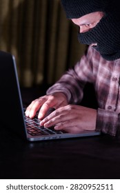 Computer hacker wearing a mask using a laptop for data breach and cyberattack