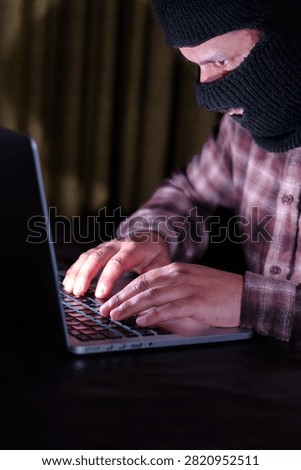 Computer hacker wearing a mask using a laptop for data breach and cyberattack