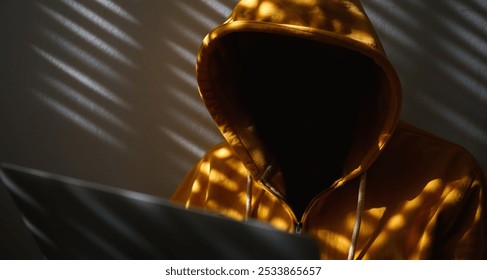 Computer hacker wearing yellow hoodie using laptop, selective focus