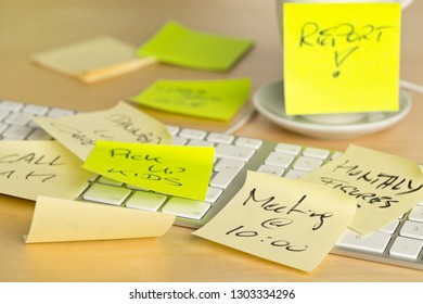 Computer keyboard and coffee cup covered with sticky notes with different appointments on brown wooden desk in office - over-worked or too much work concept - selective focus