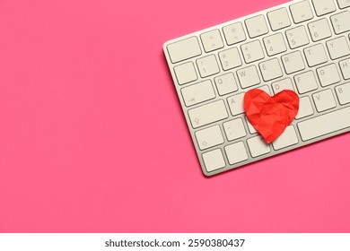 Computer keyboard with crumpled paper heart on pink background. Concept of online dating