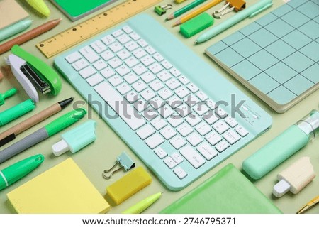 Computer keyboard and different school supplies on green background, closeup
