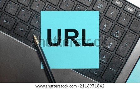 The computer keyboard has a pen and a blue sticker with the text URL Uniform Resource Locator. Flat lay.