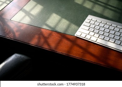 Computer keyboard on wood and leather table. Light play forming lines and shadows. Copy space.