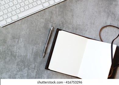 Computer keyboard, pen and notebook on concrete desk