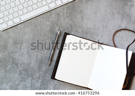 Computer keyboard, pen and notebook on concrete desk